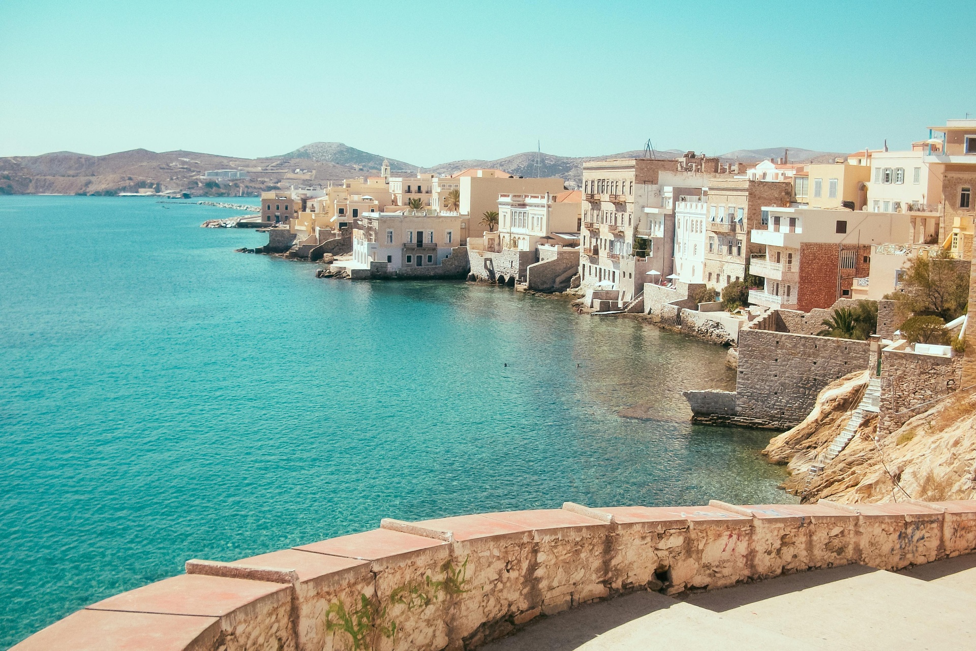 Coastal view of Syros, Greece — turquoise Aegean water meeting pastel neoclassical houses along the shore